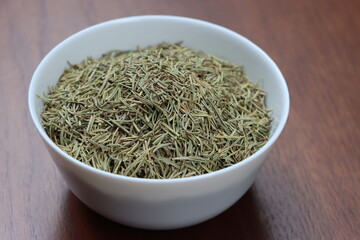 Rosemary or Salvia rosmarinus, dry leaves in white bowl, herb and seasoning
