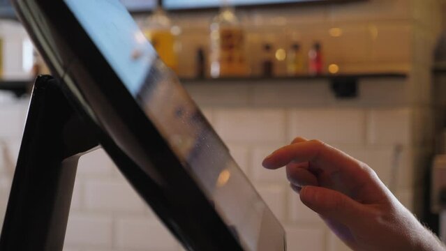 A close-up of a waiter or bartender working at a computer in a cafe, he clicks on the touch screen and places an order. The waiter works with an electronic panel for orders and receipts.