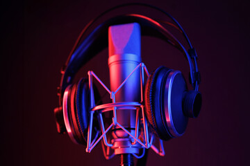 A close-up of a microphone and headphones for podcasting or ASME sounds on black stand in a neon led lighting, cyan and magenta, in a sound recording studio - Powered by Adobe