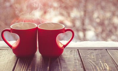 two heart shaped mugs with tea on the background of a window in winter
