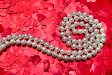 Pearl necklace on a background of red hearts
