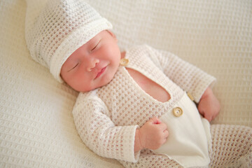 Cute newborn baby wearing a white suit is sleeping on a white blanket. A very adorable smile...