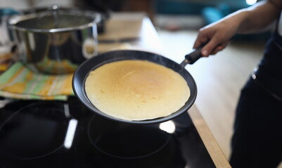 Hand holds pan with pancake, cooking at home. Available products, home recipes. Main types breakfast. Rules for working with toppings and assembly popular pies. Gluten free dough