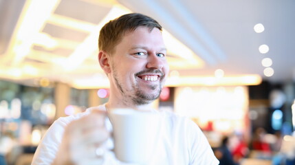 Smiling man sitting in cafe with big cup coffee. Man rejoices at opening restaurants and summer areas after pandemic. Positive attitude person. Emotional lift from an evening walk