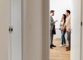 A young, beautiful, cheerful couple expecting a baby, talking with a real-estate agent visiting apartment for sale or for rent. Future parents buying an apartment. Real estate concept. A new beginning