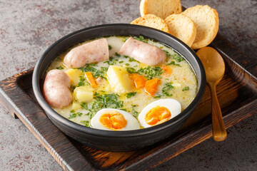 Zurek Traditional Polish soup on rye sourdough with sausage and egg close-up in a bowl on the table. Horizontal