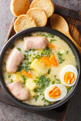 Zurek or Zur is a sour soup made of vegetables, sausages and a fermented rye flour starter close-up in a bowl on the table. Vertical top view from above