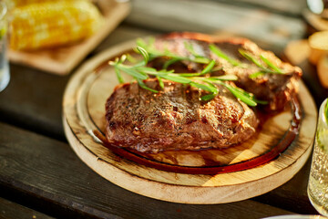 A succulent ribeye steak, perfectly grilled and adorned with fresh rosemary sprigs, rests on a circular wooden plate against a dark, rustic backdrop.