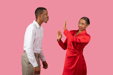 Black man blowing kiss to woman who gesturing stop, pink background