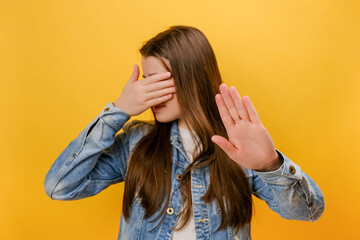 Portrait of young woman keeping hand on eyes, grimacing in disgust and turning away from camera, avoiding watching something shameful, posing isolated over yellow color background wall in studio - obrazy, fototapety, plakaty