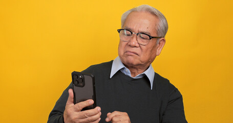 An old Asian man expressed his displeasure when he saw something on his phone. Isolated on yellow...