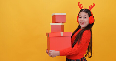 Cute little girl wearing a Christmas costume holding gift boxes. Isolated on yellow background in studio.