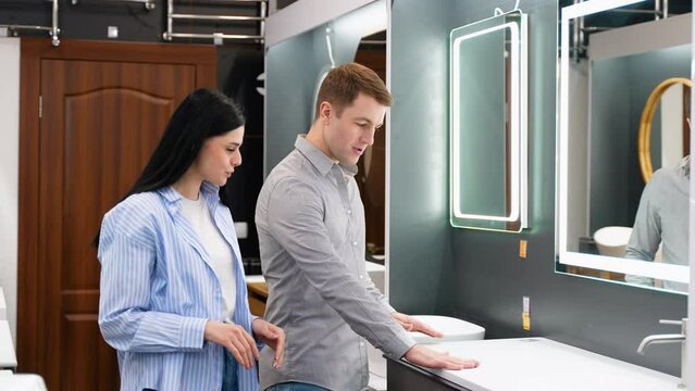 Young couple choosing new bathroom furniture at the plumbing shop with lots of sanitary goods