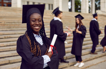 Portrait of happy female student with diploma on graduation day. Beautiful young African American...