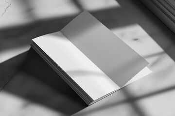 A white book sits on top of a table next to a window. This versatile image can be used for various themes and concepts