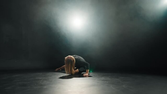 Middle aged woman choreographer dancing. Blonde female ballerina dances in black dress in studio on black background. Perform dance element of classical ballet. Rehearsal choreography concept.
