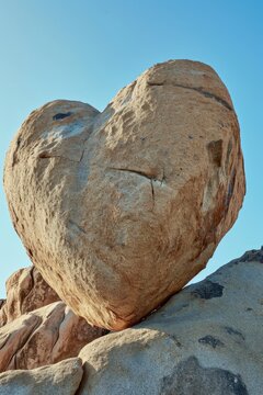 A heart shaped rock sits on top of a large rock. This image can be used to symbolize love and affection.