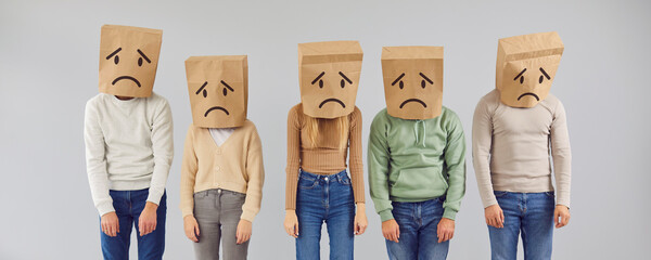 Five casual people incognito personalities with psychological diseases and disorders wearing brown package bags over heads with drawn sad depressed mouth and eyes standing in light gray color studio - obrazy, fototapety, plakaty