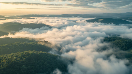 Fototapeta premium Aerial forest mountains landscape in the morning gold light with lots of low clouds into the valleys and a hazy sky