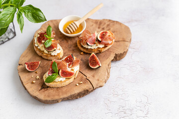 Bruschetta with prosciutto, creme cheese, figs, basil and walnut and honey on a wooden board. Antipasti, canape, crostini recipe, restaurant menu. Tasty breakfast. Side view, copy space.
