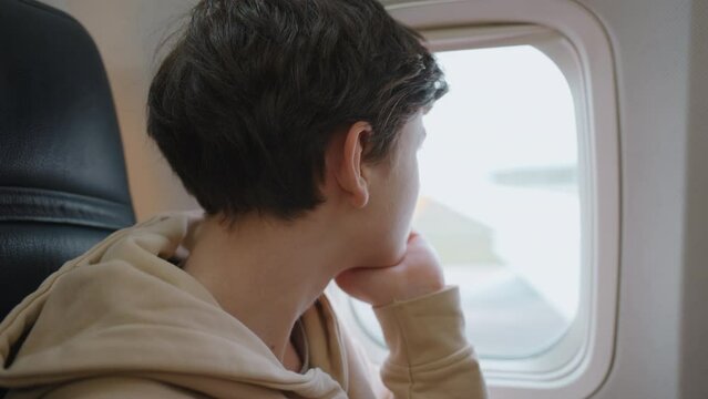 Tourist male looking with interest out window of porthole in an airplane with interest watching runway taking off plane window. Family travel by airplane in summer. Travel concept