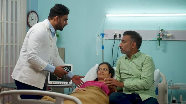 Indian doctor speaking with patients husband about medical condition at hospital ward - concept of professional advice, discussion and comforting