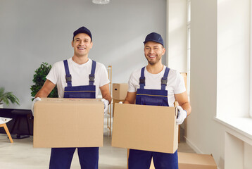 Portrait of a two young male happy smiling employee of moving service in overall standing in the...