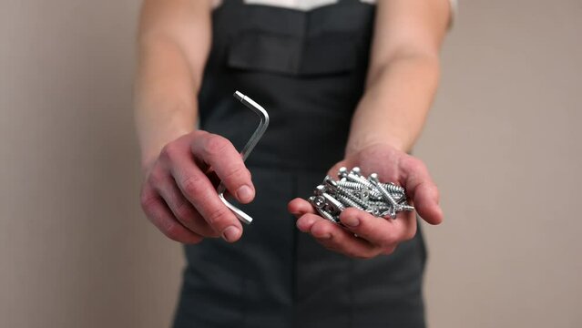 Furniture assembler holds countersunk screws and a hex wrench in his hand, close-up. Construction concept, handyman,furniture assembly.