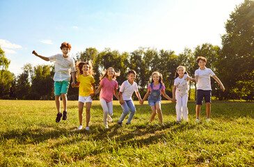 Group of a smiling kids friends jumping with hands up on green grass in the park standing in a...