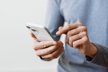 Closeup of adult male hand using mobile phone, Young man texting on smartphone over grey background.