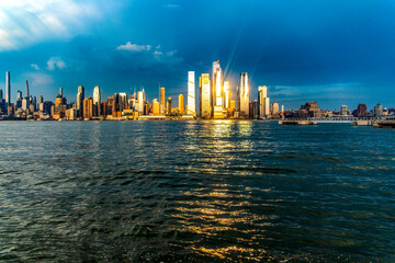 Skyline of New York and the Big Apple seen from a viewpoint on the Hudson River, under a sunset and the sun's rays reflecting on the buildings.