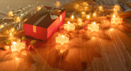 Red gift box and candlelight on a wooden table.