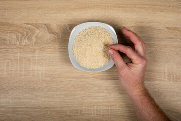 Hand Picking up Rice from White Bowl - Hunger, Food and Agricultural Greenhouse Gas Emissions Concept.