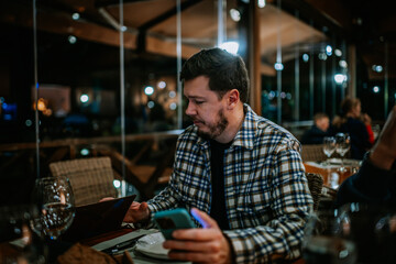 Malaga, Spain - January, 21, 2024 -  man in a plaid shirt looking at his smartphone in a restaurant...