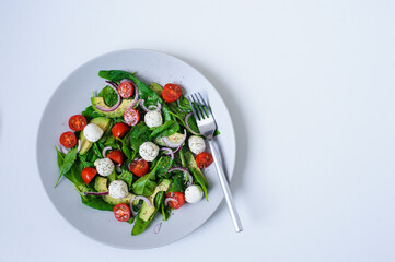 delicious diet salad  with cherry tomatoes, avocado, spinach leaves, Mozzarella and red onion with olive oil dressing served on plate on white background