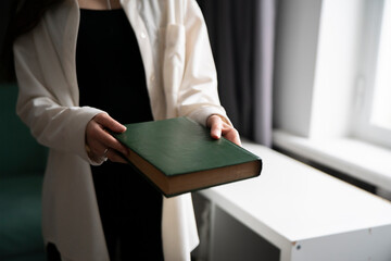 Close-Up of a Person's Hands Offering a Green hardcover Book Indoors