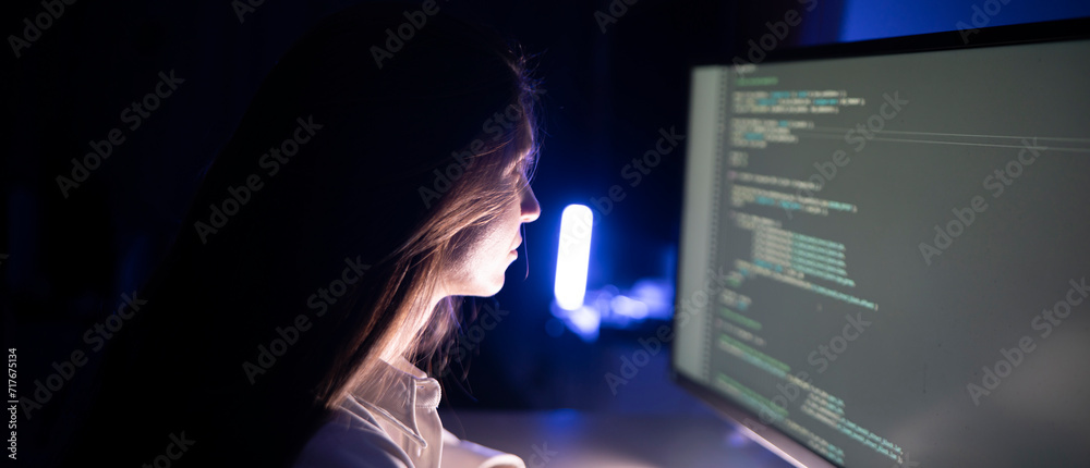 Wall mural a focused woman works diligently on her coding assignment in front of a computer screen in a dimly l