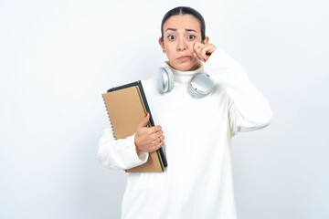 Disappointed dejected Young beautiful woman wearing white turtleneck sweater wipes tears stands stressed with gloomy expression. Negative emotion