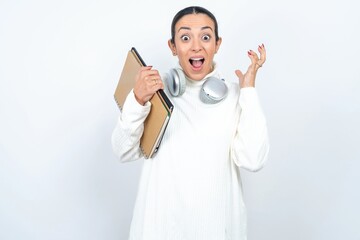 Surprised happy Young beautiful woman wearing white turtleneck sweater, glad to see big discounts on clothes, expresses shock, keeps hands near head, jaw dropped.