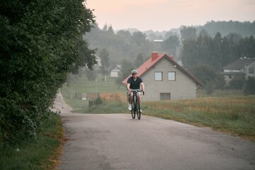 A young and fit cyclist on a bicycle explores the country landscape, riding on a road in the forest with a helmet and a mountain bike. Gravel biker on a path, enjoying the sport and the nature.
