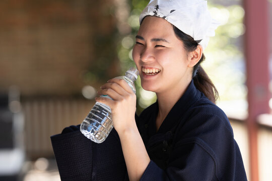 剣道の道着姿で水のペットボトルを持って笑っている女性剣士
