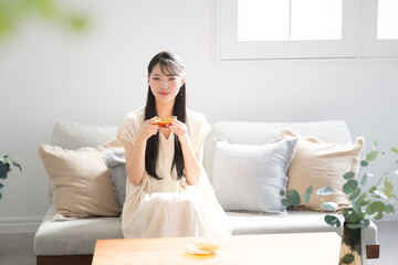 Asian (Japanese) woman with long hair relaxing in room, drinking tea, looking at camera