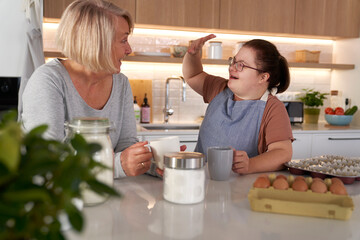 Down syndrome woman and her mother chatting in the kitchen