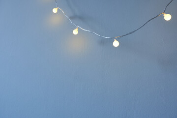 Glowing garland on blue wall background, selective focus. Free space for copying. Concept - cozy...