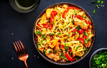 Stir fryed egg noodles with chicken, pineapple, paprika, green onion, soy sauce and sesame seeds in bowl. Asian cuisine dish. Black table background, top view
