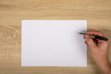 Obraz premium Creative Workspace: Top-Down View of Hand Drawing with Pen on Horizontal White Paper on Wooden Table, Copy Space