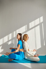Two young women doing yoga meditation. Concept of physical and mental health care, asian and caucasian ethnicity