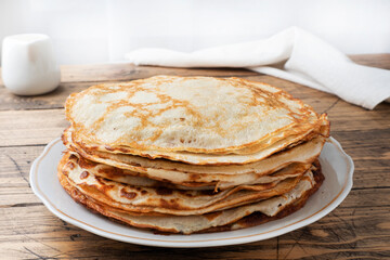 Thin pancakes on a plate, wooden background. The concept of a delicious breakfast or Maslenitsa