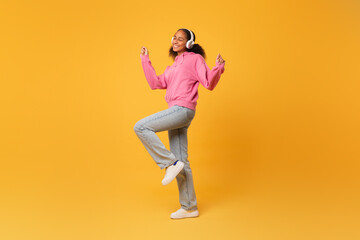 Fototapeta na wymiar black girl in headphones listens music dancing over yellow background