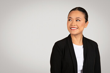 Optimistic Asian businesswoman in a black suit looking away with a pleasant smile